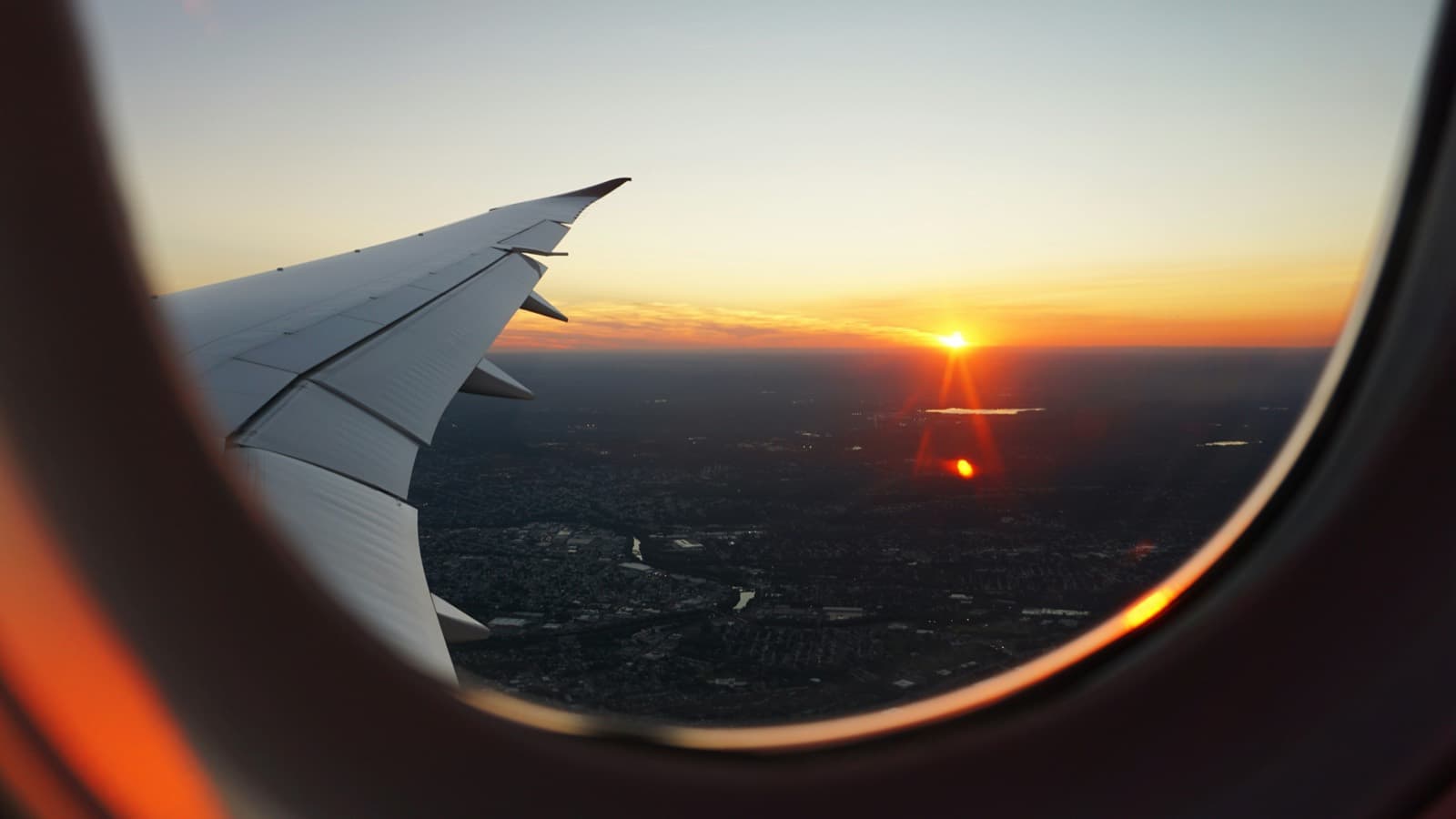 Airplane window view of a city at sunset, arriving as an international